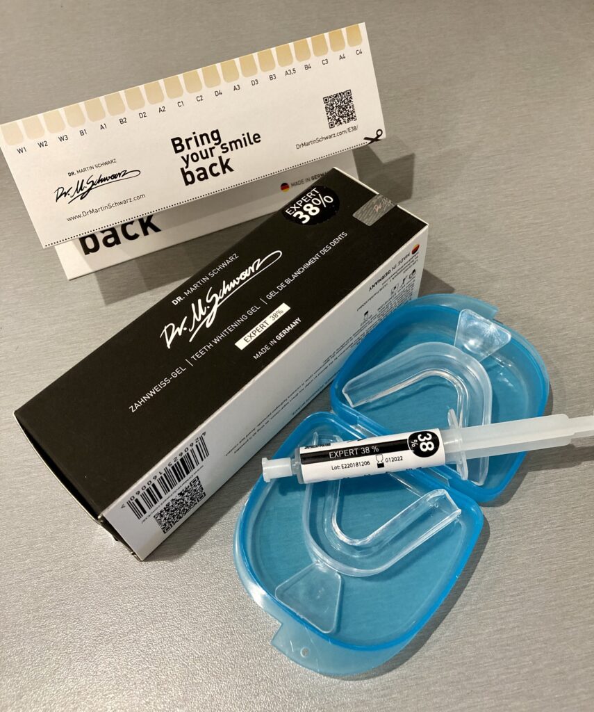 The black box next to a syringe of clear teeth whitening gel on top of the mouth tray 
