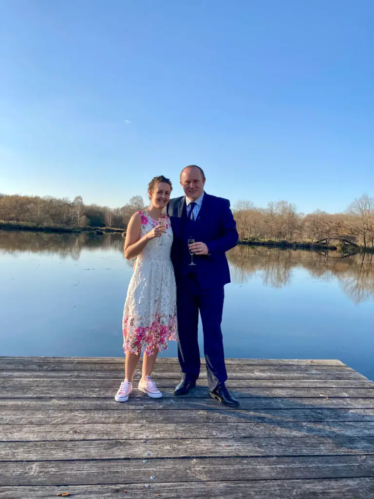 D and I standing together at the end of the decking by a lake. I’m wearing a white and pink dress and Dan is wearing a navy suit 