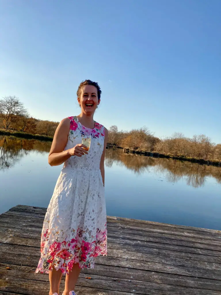 I’m standing by a lake in a white dress with pink flowers on it. I’m laughing and holding a glass of champagne 