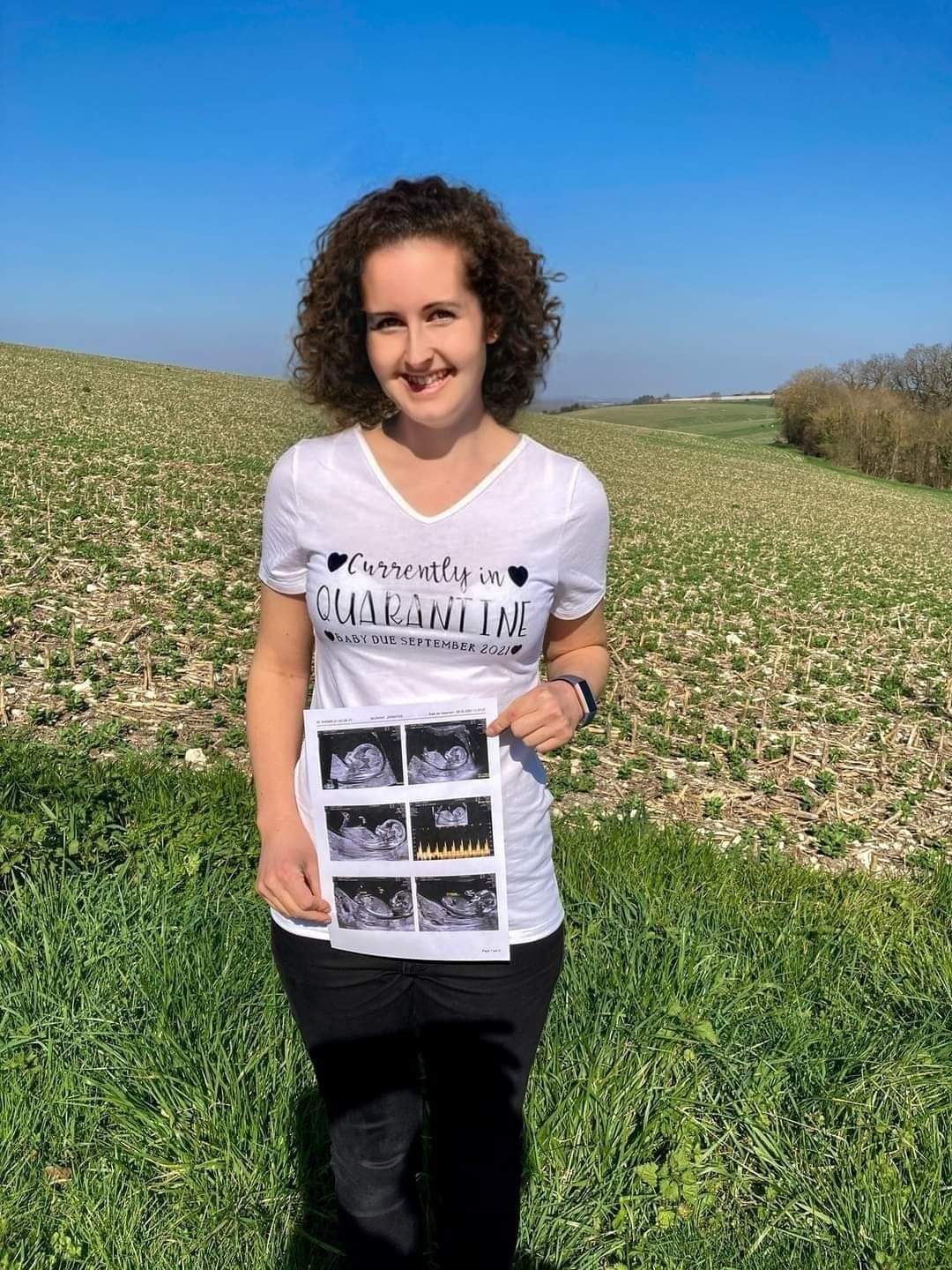 I’m holding up scan photos wearing a white Tshirt saying baby due September