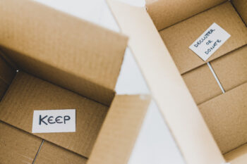 decluttering and tidying up conceptual still-life, white storage boxes to sort between objects to keep and those to declutter or donate with respective labels
