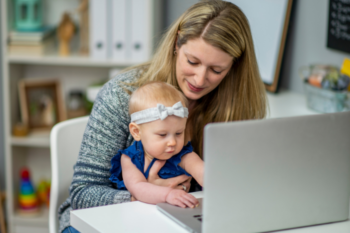 a ;ady working at a laptop holding a baby