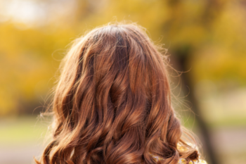 the back of a ladies head with aubern hair and the background is autumn trees