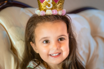 a girl with dark hair wearing a pink and gold birthday crown with 3 on