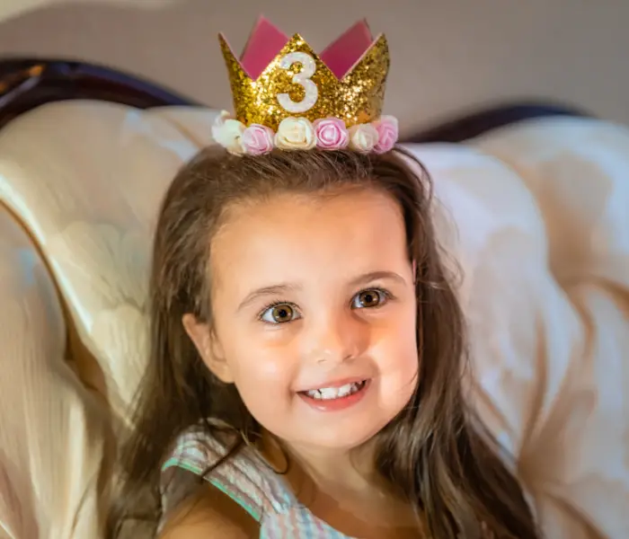 a girl with dark hair wearing a pink and gold birthday crown with 3 on