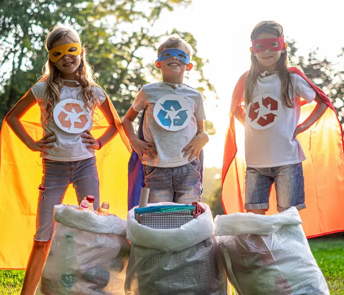 three children wearing superhero masks and capes and recycling signs on their tshirts as they stand next to recycling bags