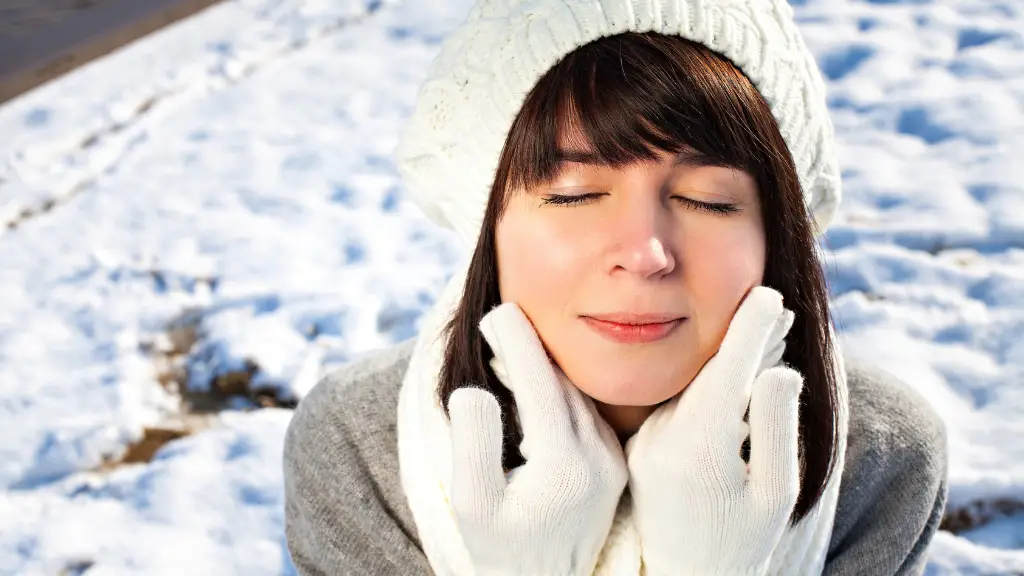 winter skincare. a lady wearing a white hat and gloves touching her face. The background is snowy