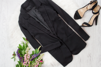 a flatlay with a longline black blazer, black heels and flowers