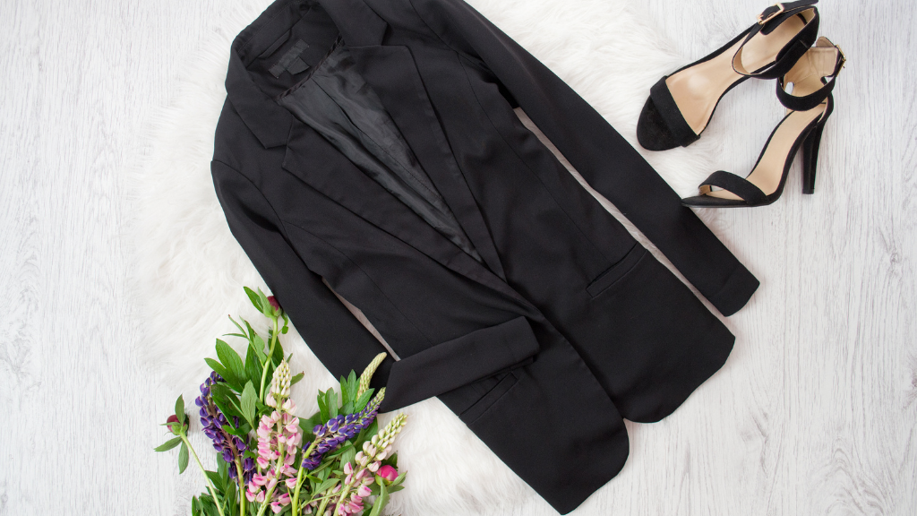 a flatlay with a longline black blazer, black heels and flowers
