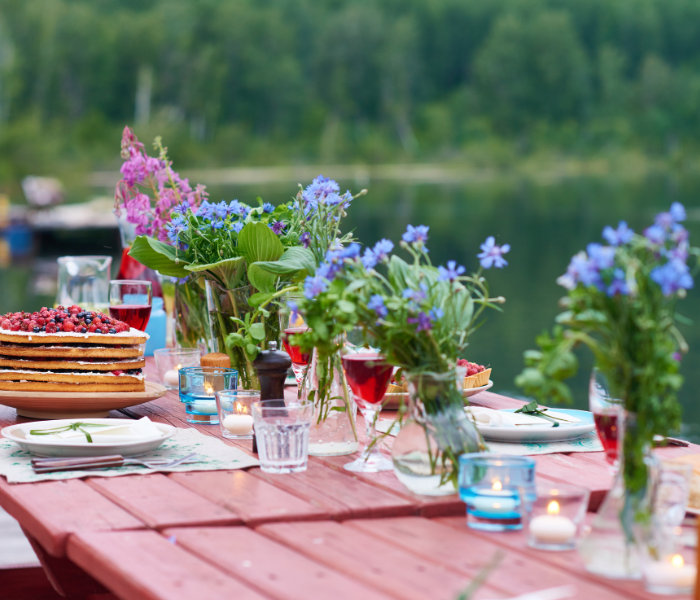 garden party. a table is set outside with tea light candles, flowers in vases and a cake
