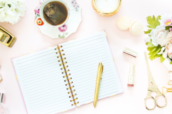 a notebook, stationary, candles and cup of tea on a desk. balancing motherhood and entrepreneurship working from home