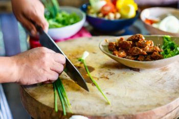 someone chopping spring onion on a chopping board and curry in front of them in a bowl