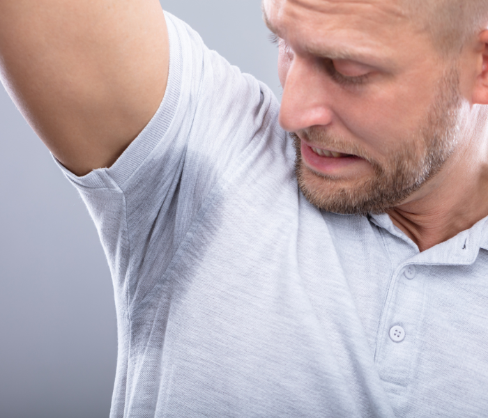 man looking at his underarm showing sweat through his tshirt