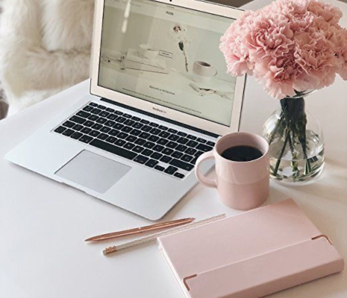 laptop next to a cup of coffee, pink notebook and pink flowers in a glass jar