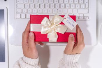 a pair of hands holding a gift wrapped in red paper with a white bow and a label saying secret santa
