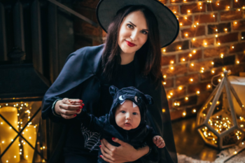 a lady and baby in halloween costumes, she is wearing a witches outfit, the baby is wearing a black outfit