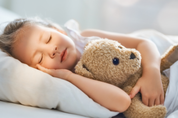 child sleeping on a white pillow, holding a stuffed teddy