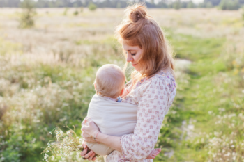 a lady stood in a field with her baby in a wrap on her chest