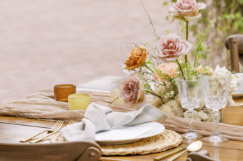 a table set with plates, napkins and gold cutlery. Cream and pale pink roses are in a glass jar
