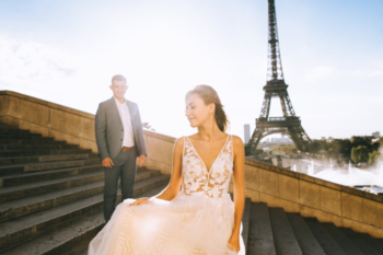 a couple with Eiffel tower in the background. the lady is wearing a wedding dress and the man is in a suit