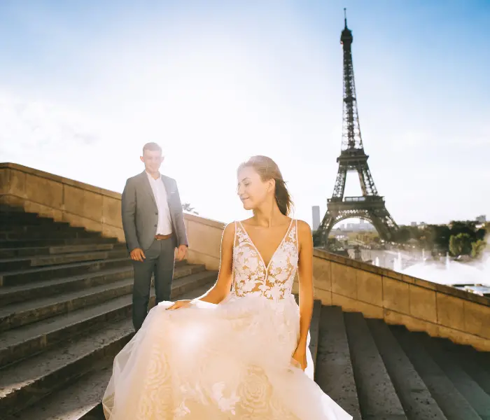 a couple with Eiffel tower in the background. the lady is wearing a wedding dress and the man is in a suit