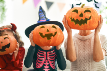 lady and 2 girls dressed in halloween costumes holding up pumpkins covering their faces