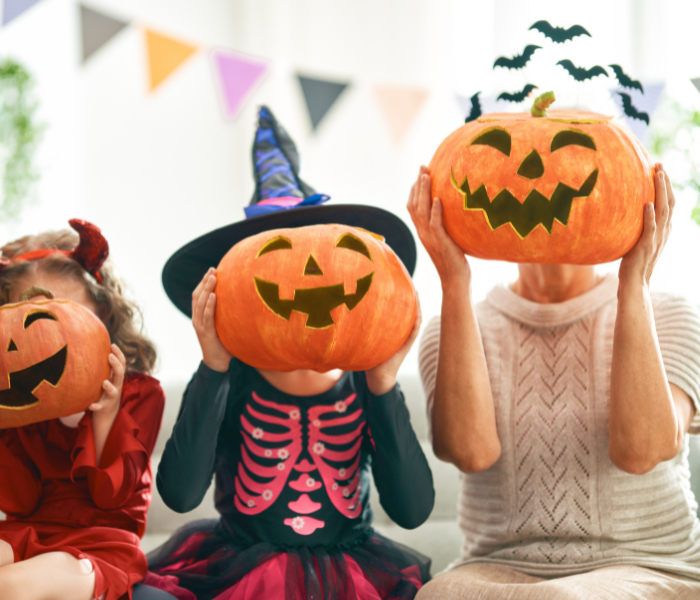 lady and 2 girls dressed in halloween costumes holding up pumpkins covering their faces