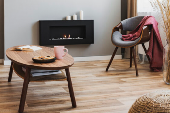 living room with a fire mounted on a wall, vinyl flooring, grey chair and wooden table. modern but comforting look