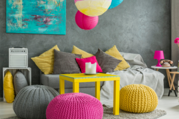 a room with grey walls and sofa with bright accessories, bright yellow and pink cushions, blue wall art