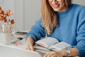 lady on laptop. she has blond hair. wearing a blue jumper and silver watch