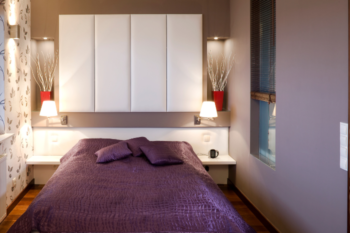 small bedroom with a double bed in and storage above. purple colour decor