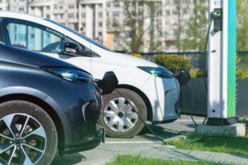two electric cars parked up charging with building bahind