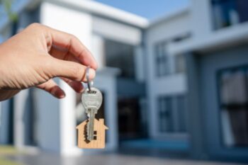 a hand holding out a key in front of a house