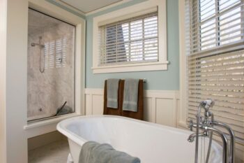 bathroom showing a bath and shower. there are two windows with white blinds