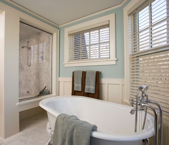 bathroom showing a bath and shower. there are two windows with white blinds