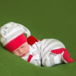 newborn baby in white and grey stipy baby grow and hat with red edging. bbay is asleep on green blanket