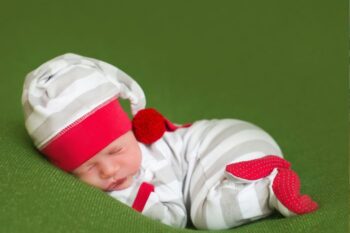 newborn baby in white and grey stipy baby grow and hat with red edging. bbay is asleep on green blanket