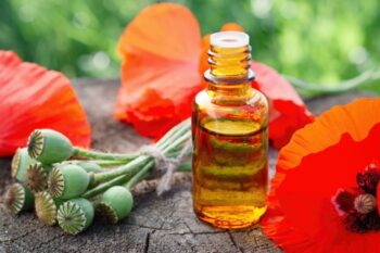 a small bottle of oil next to poppies