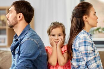 man and lady with backs to each other with a child sat in the middle with her hands on her face