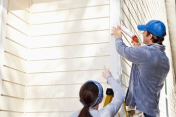 a man doing work to the side of a house with a lady pointing