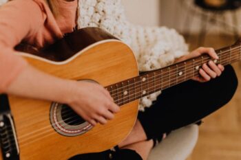 close up of guitar, you can see a ladies hand playing and she is sat crossed legged with it on her