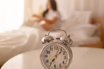 alarm clock in focus with a lady in the background sat in bed out of focus
