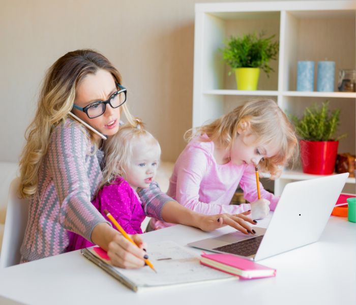lady with laptop in front of her, shes on the phone and has 2 kids on her knee