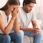 a man and woman sat next to end other looking upset and tense