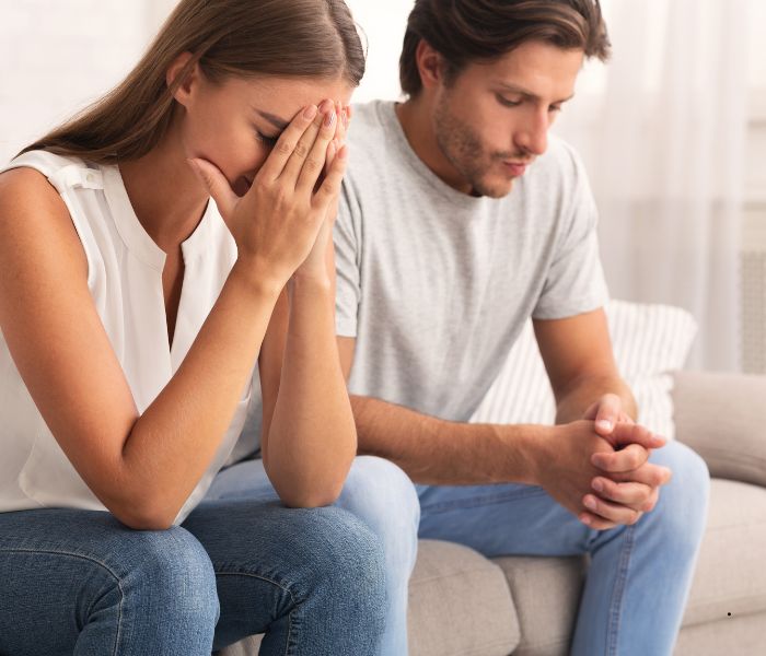 a man and woman sat next to end other looking upset and tense