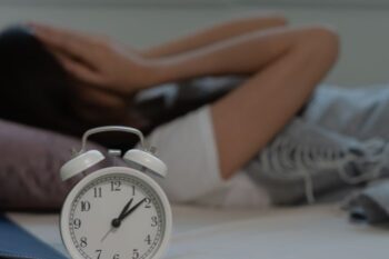 lady led in bed with hands over face and clock in forefront