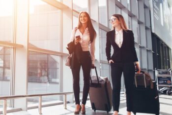 two women in business suits pulling along suitcases