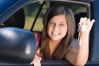 a girl sat in the car holding a key smilingat the camera