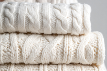 Close-up of stacked soft white cable knit sweaters, highlighting quality craftsmanship and warm, stylish winter fashion essentials.