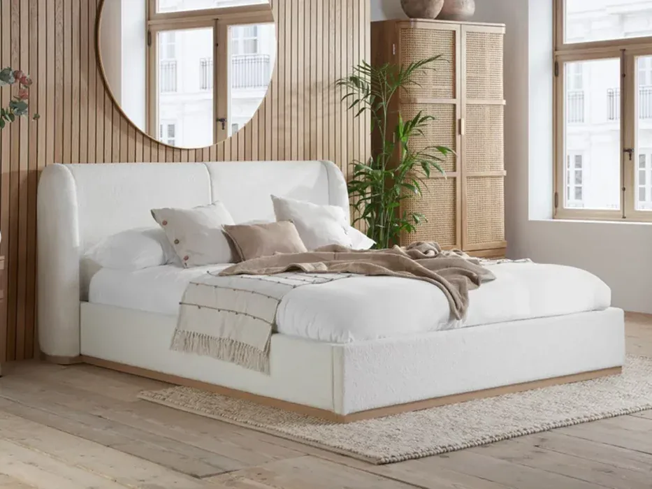 Bright and airy bedroom featuring a white upholstered bed, wooden accents, and large windows that bring in natural light, perfect for a relaxing sleep environment.